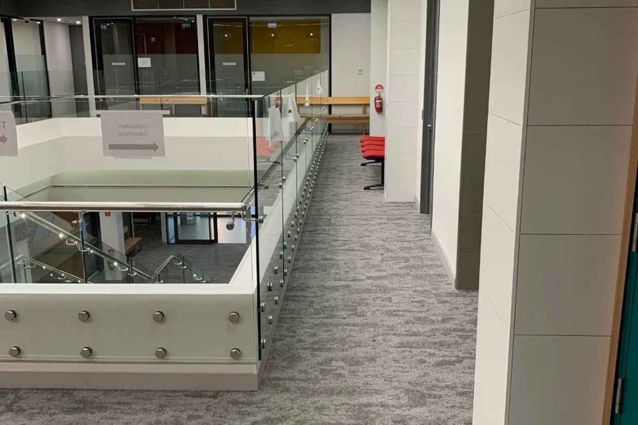 A Modern, Two-story Building Interior With a Glass Railing and Grey Carpet — Ozwide Flooring In Ciccone, NT