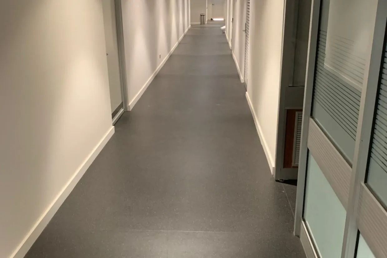 Long, Empty Office Hallway With Dark Grey Flooring and White Walls — Ozwide Flooring In Ciccone, NT