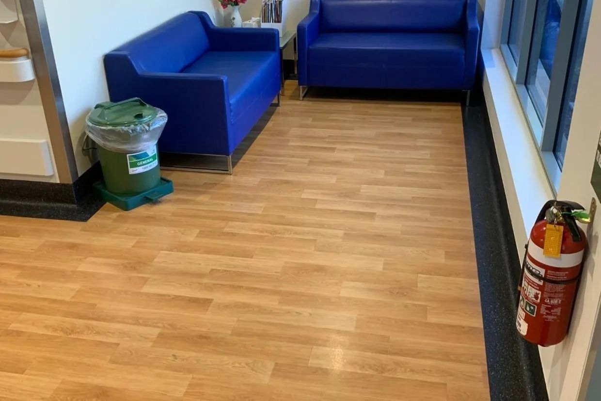 Waiting Room With Blue Couches, Wood-look Floor, Trash Can, and Fire Extinguisher — Ozwide Flooring In Ciccone, NT