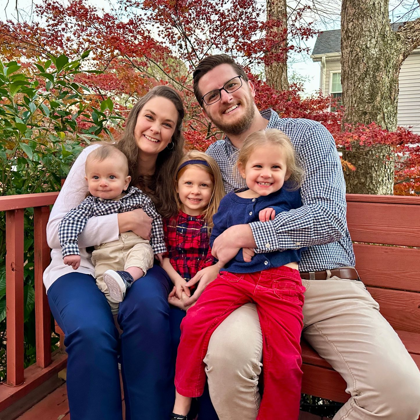 Couple smiling, sitting on a bench with their three young children sitting on their laps.