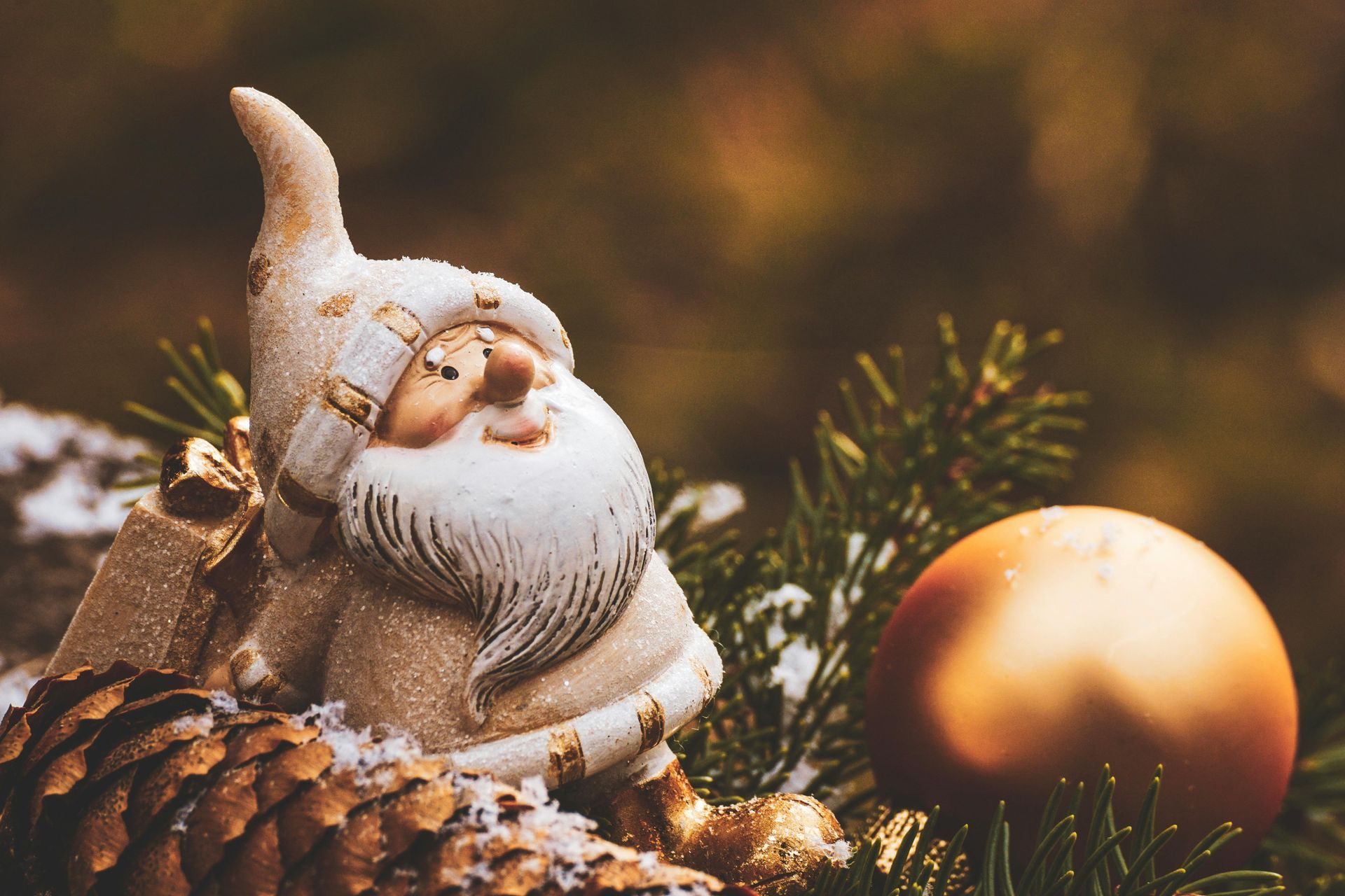 Christmas gnome figurine with a gold ornament and pine cone.