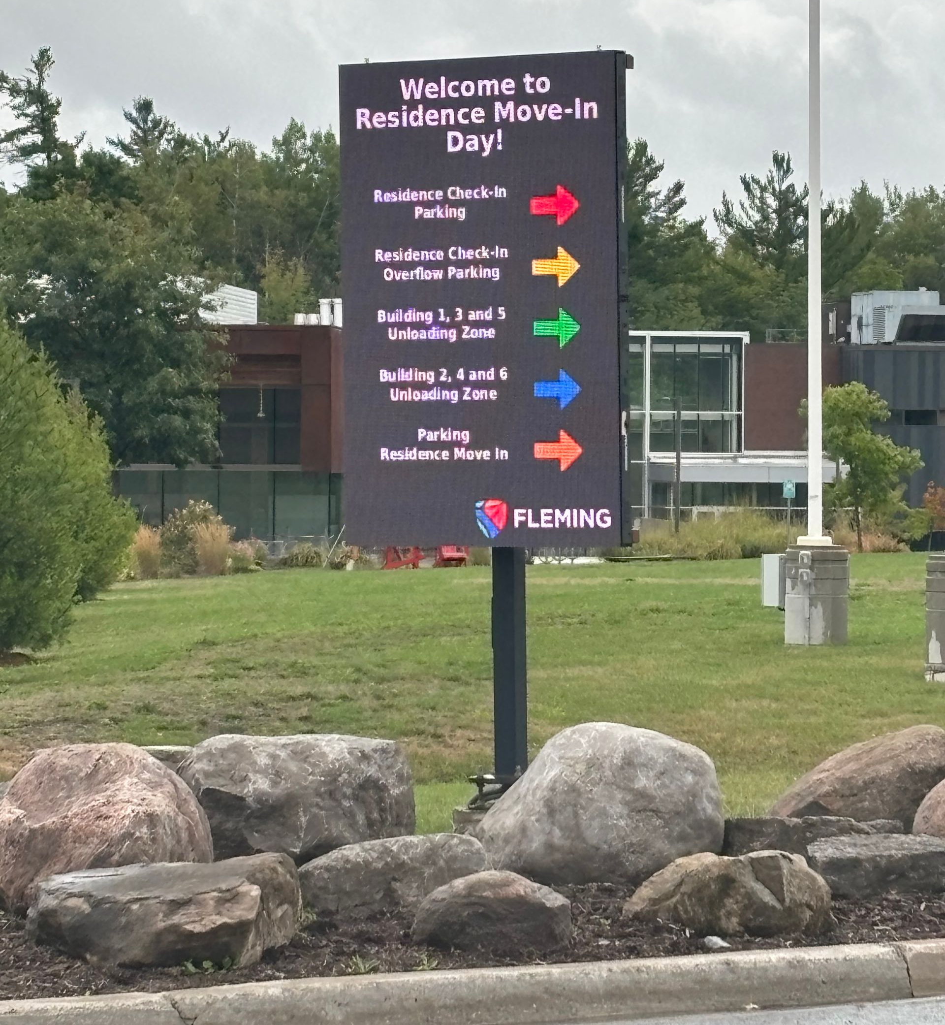 Digital sign at Fleming College giving directions for Residence Move-In Day, featuring color-coded arrows and text.