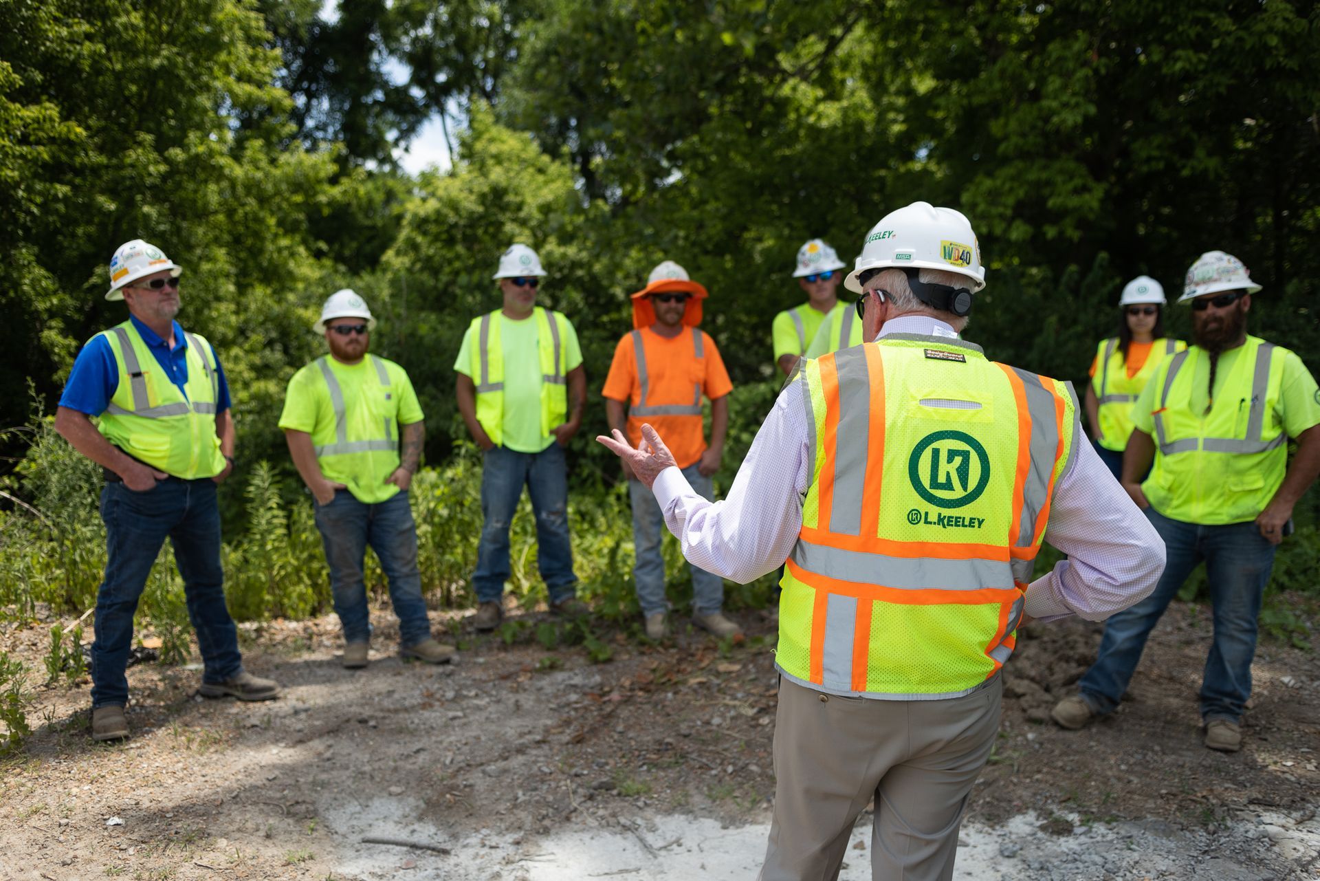 A group of construction workers wearing hard hats and safety vests are standing in a circle.
