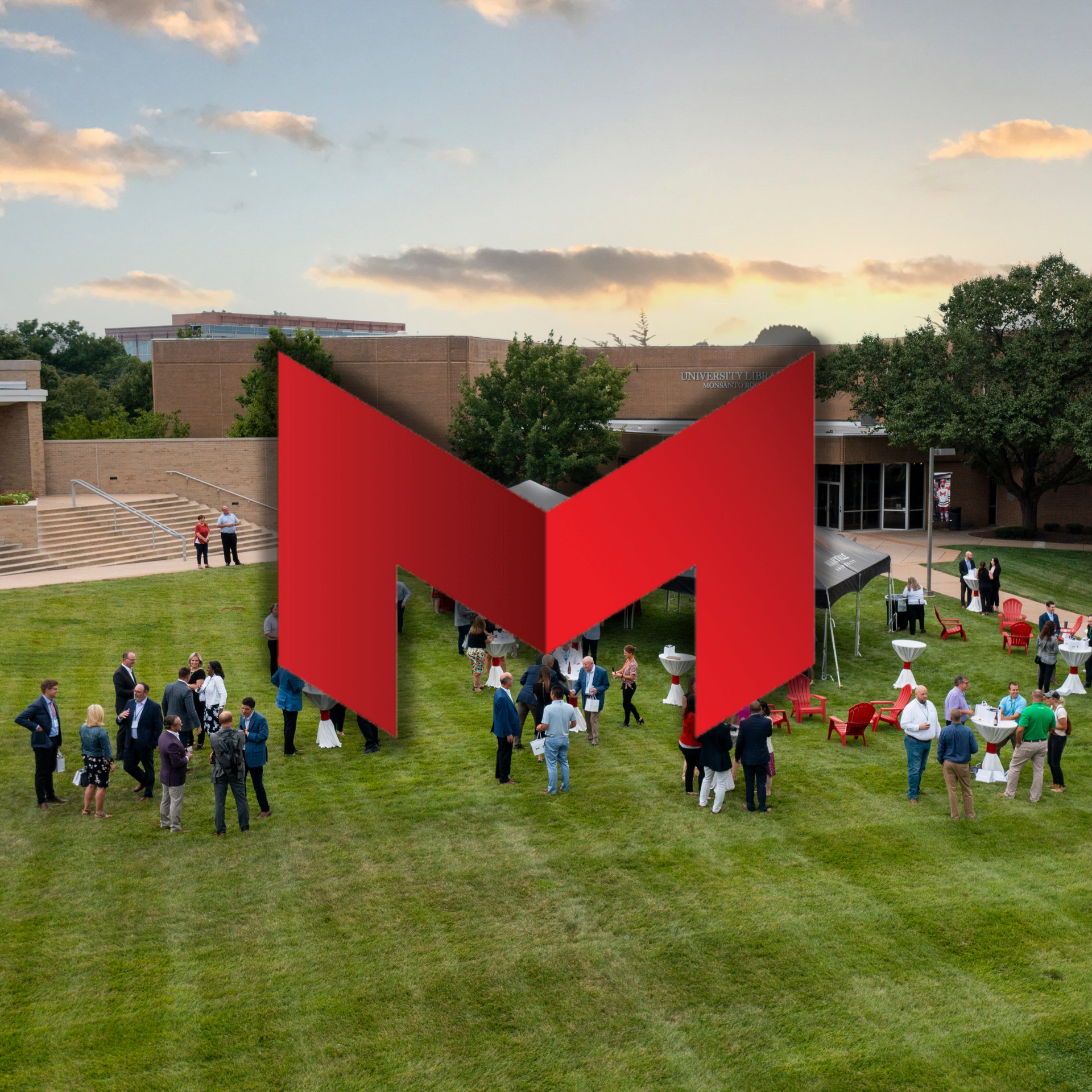 A group of people standing in a grassy field with a large red m in the background