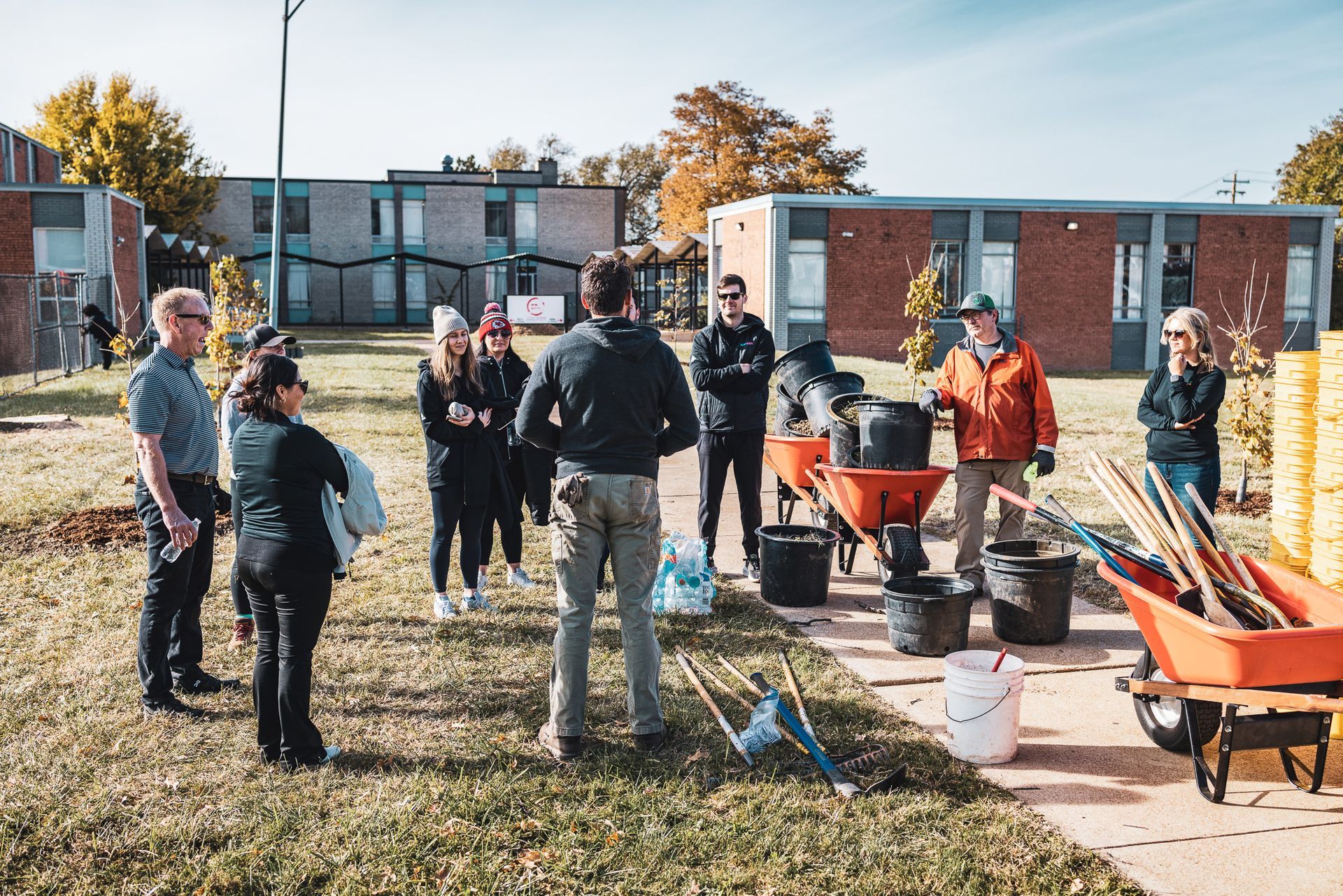 A group of people are standing around a wheelbarrow in a field.