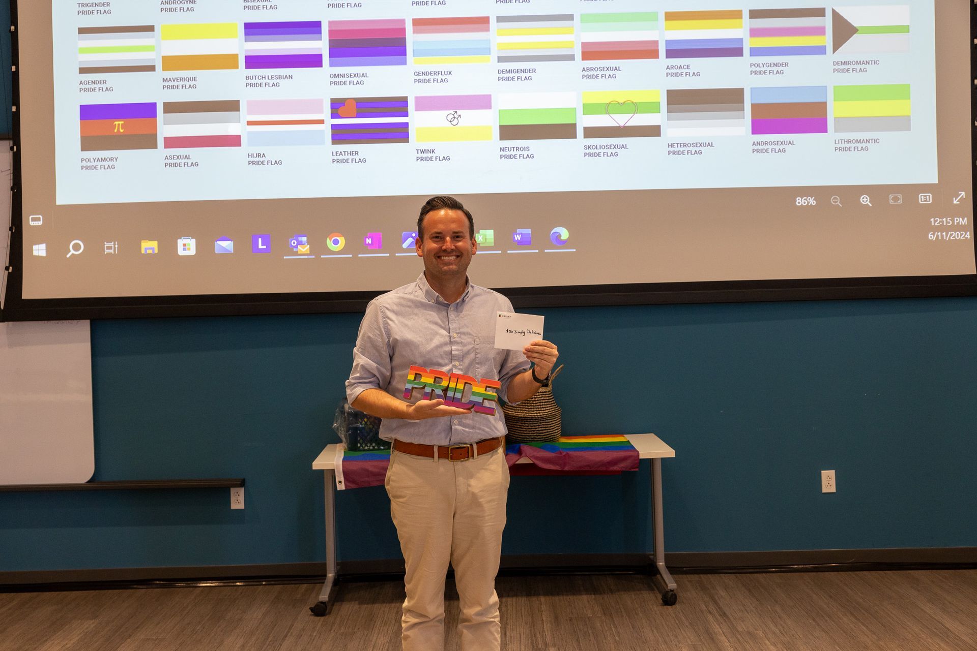 A man is standing in front of a projector screen holding a rainbow flag.