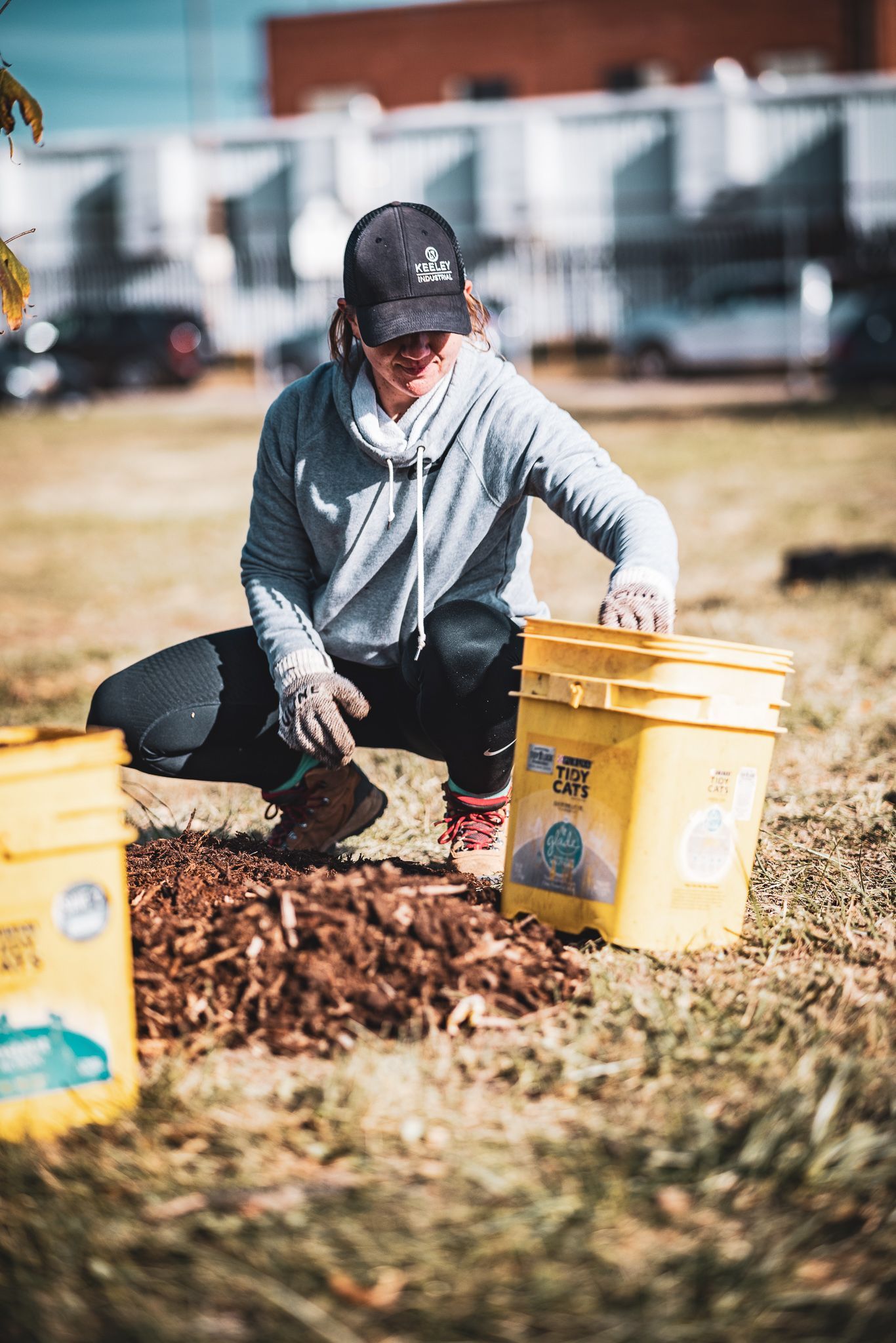 A woman is kneeling down in a field with buckets of mulch.