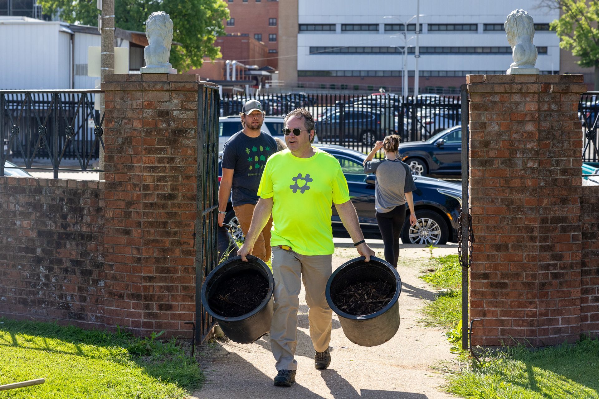 A man in a neon yellow shirt is carrying two buckets.