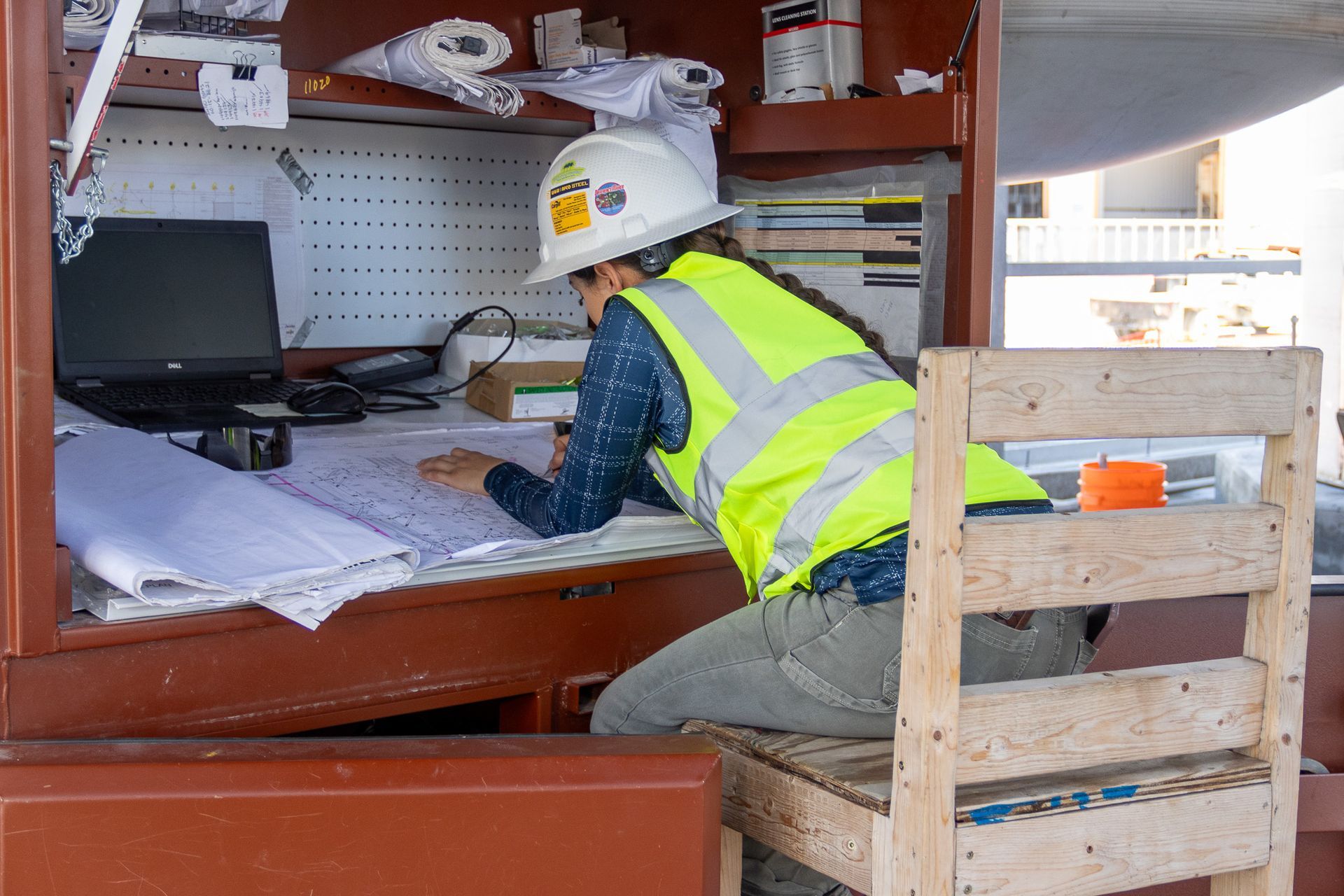 A man wearing a hard hat and safety vest is kneeling at a desk.