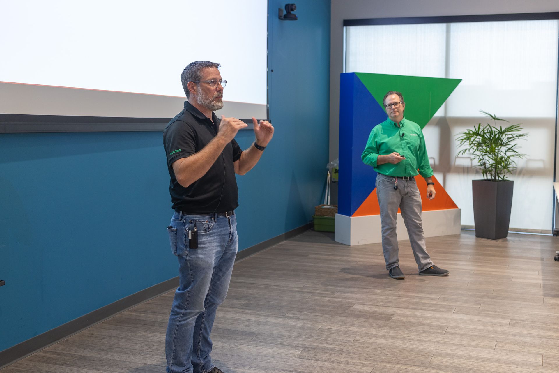 Two men are standing in front of a projector screen in a room.