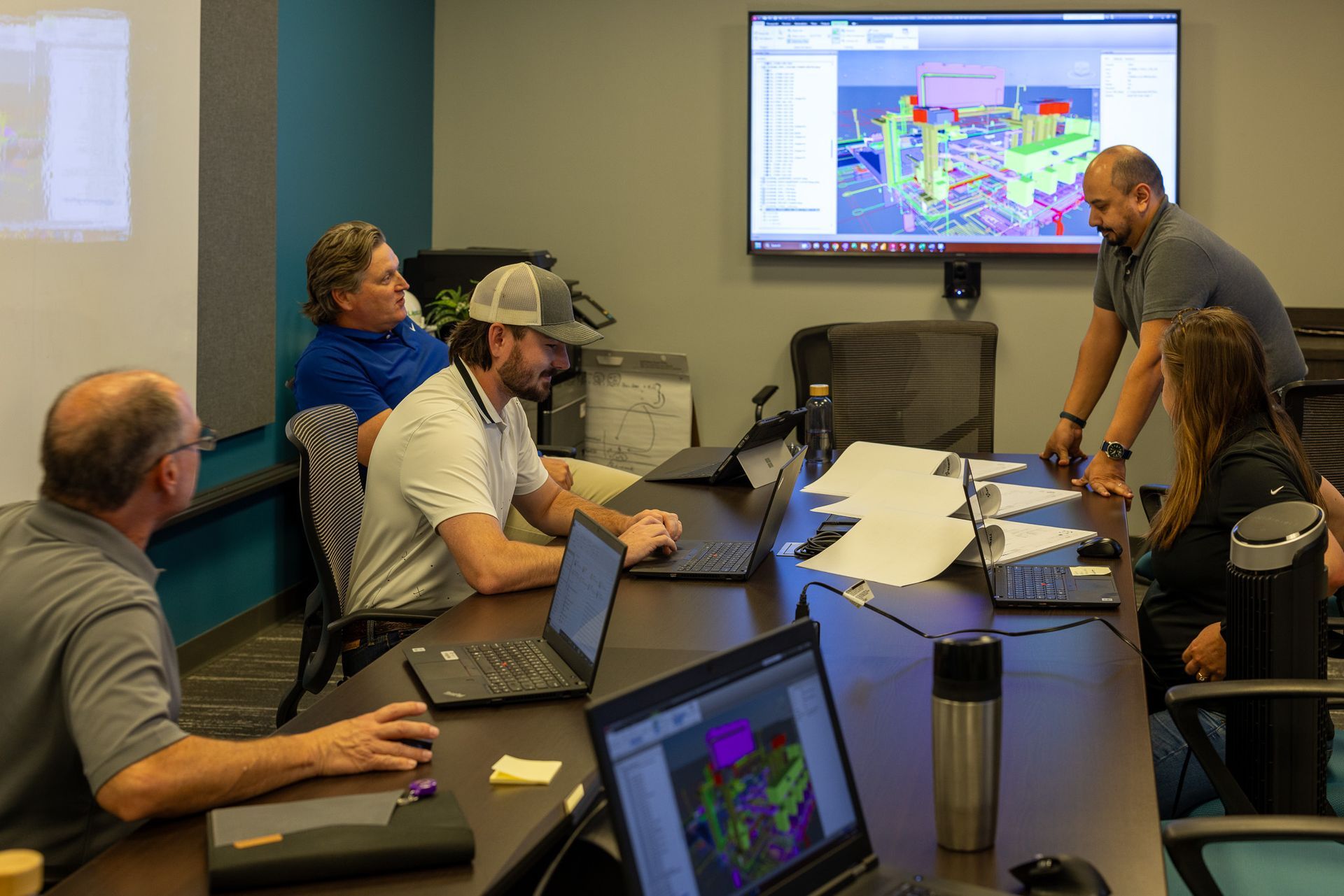 A group of people are sitting around a table with laptops in a conference room.