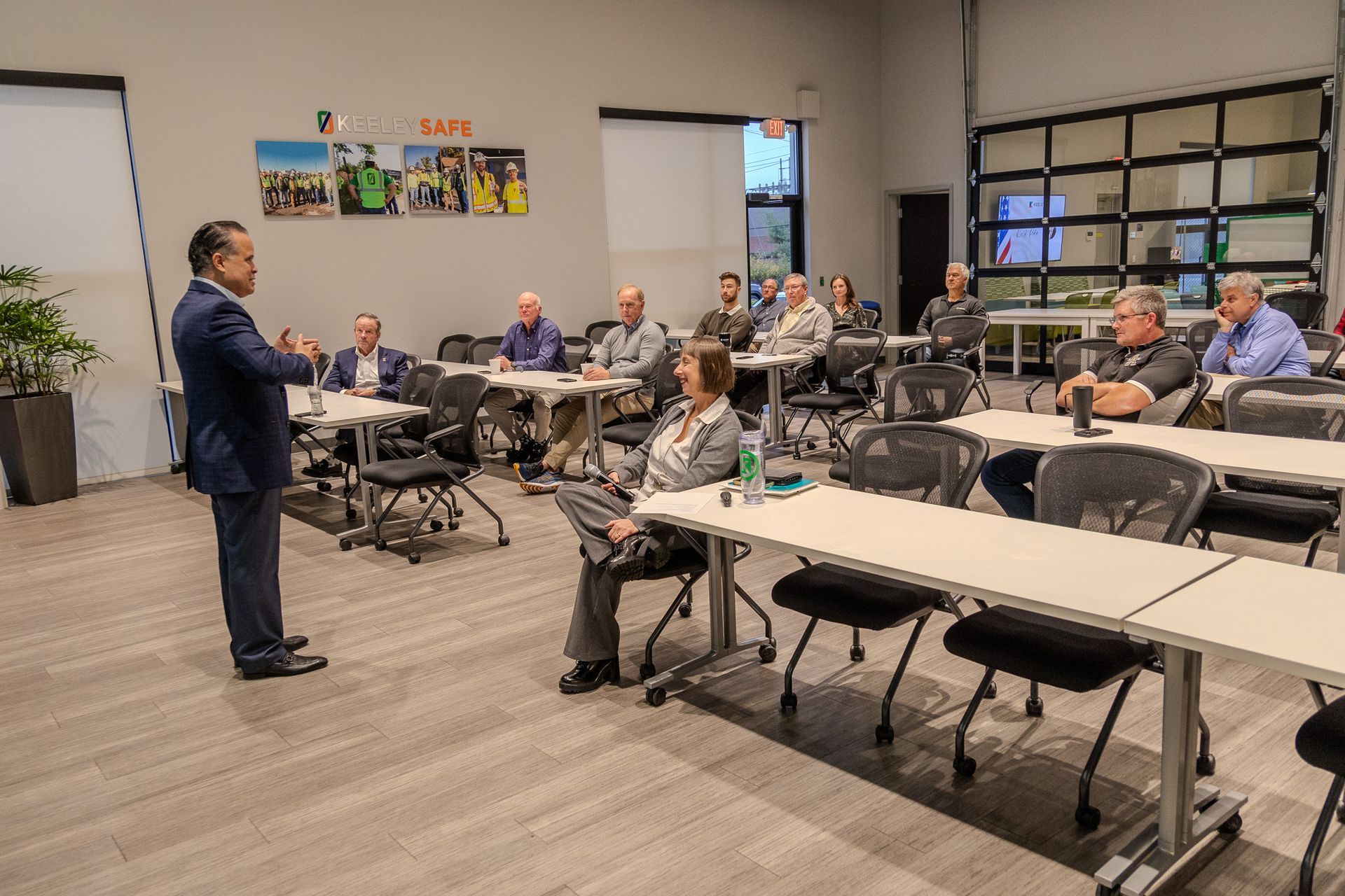A man is standing in front of a group of people sitting at tables in a classroom.