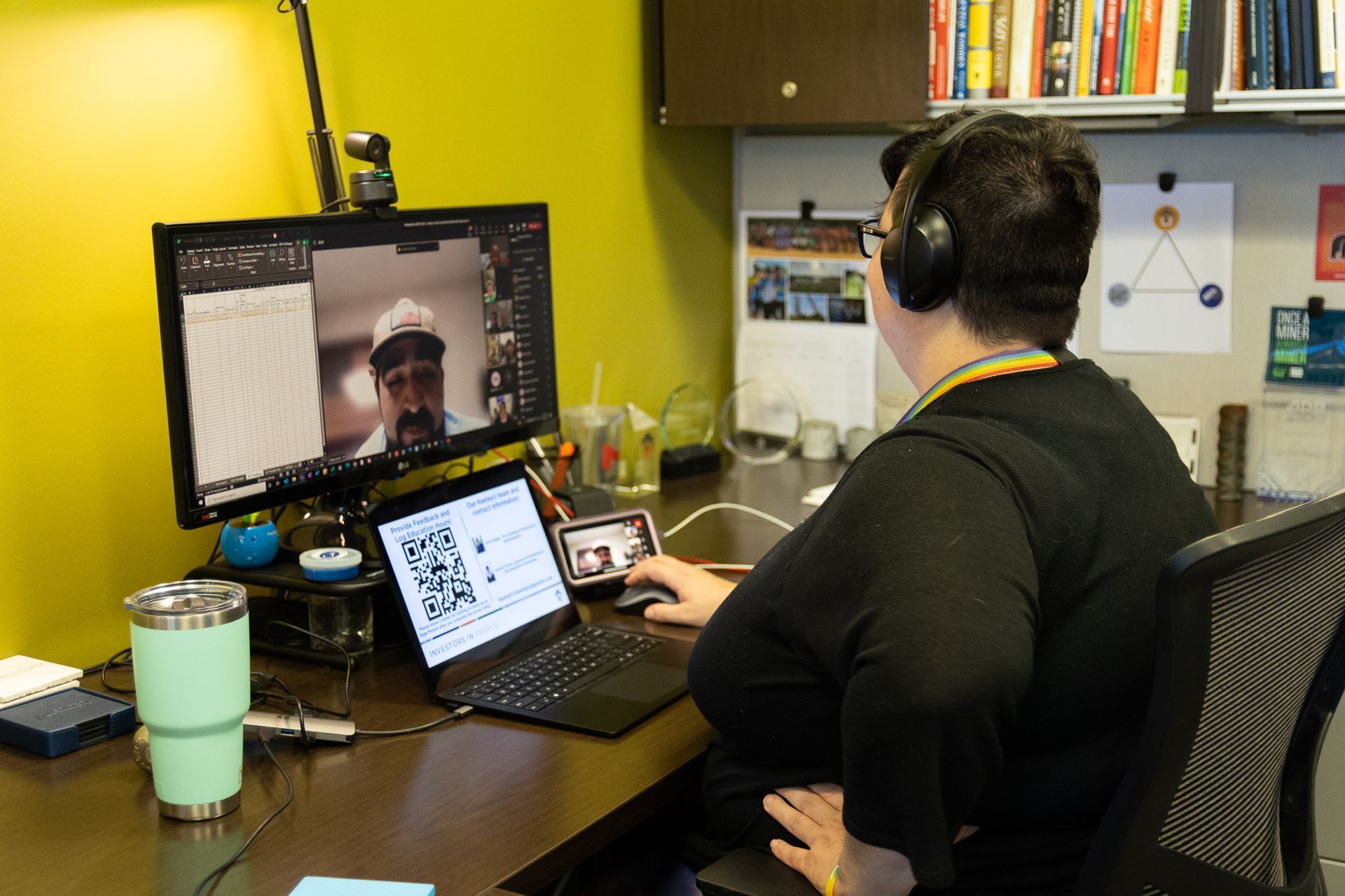 A woman wearing headphones is sitting at a desk using a laptop computer.