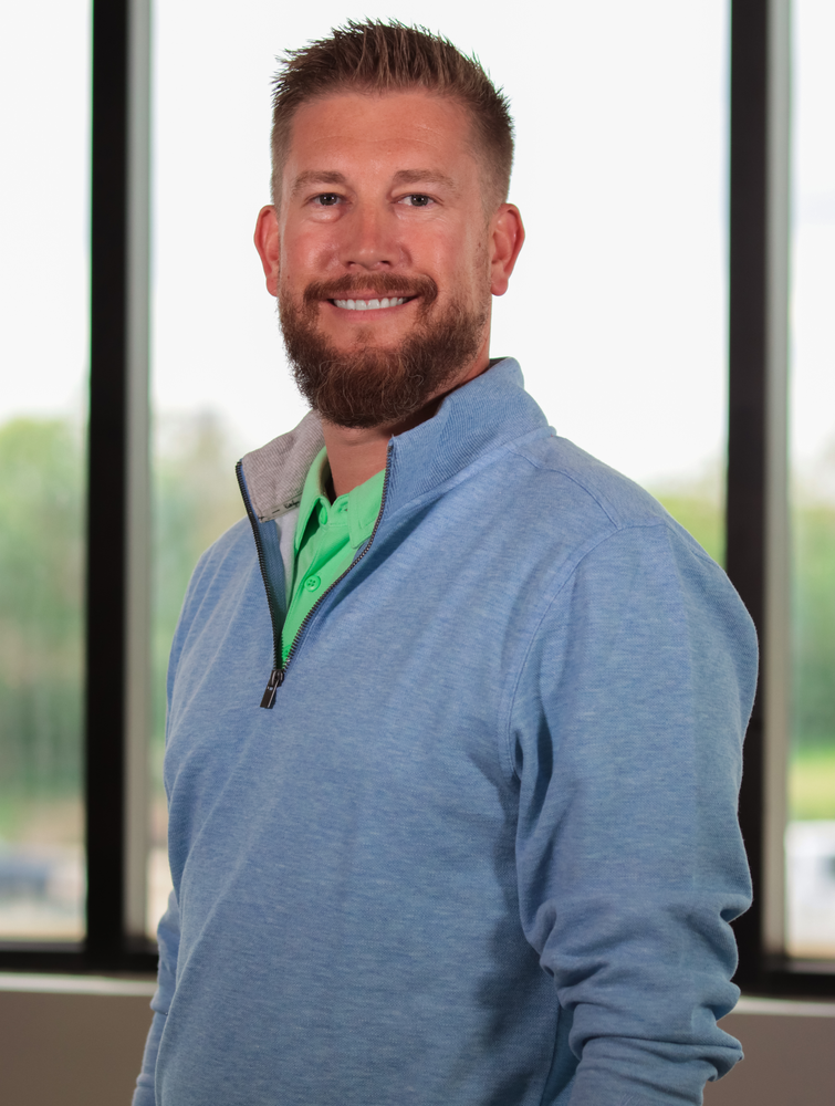 A man with a beard is wearing a blue sweater and a green shirt.