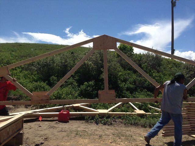 Two men are working on a wooden structure in the dirt at Pine Ridge Reservation