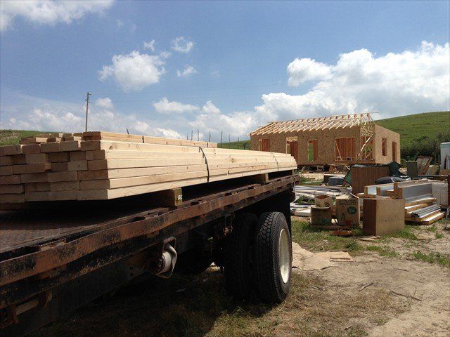 A truck is carrying a stack of wood in front of a building under construction at Pine Ridge Reservation