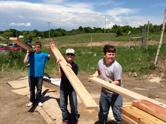 Three young men are carrying large pieces of wood at Pine Ridge Reservation