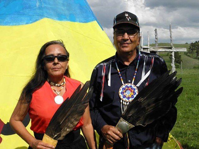 A man and a woman standing next to each other holding feathers at Pine Ridge Reservation
