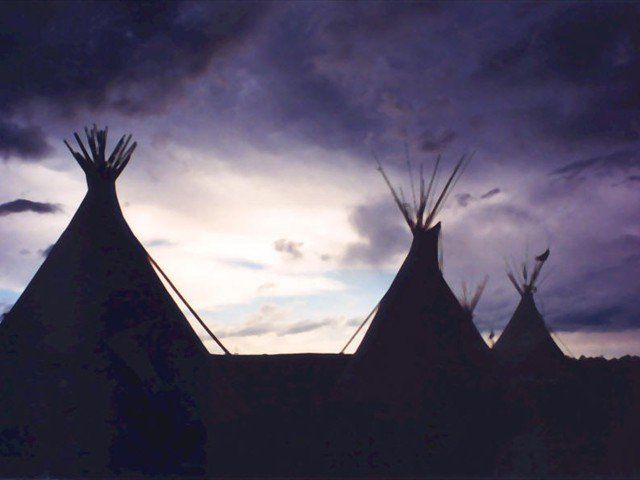 A group of teepees are silhouetted against a purple sky at Pine Ridge Reservation