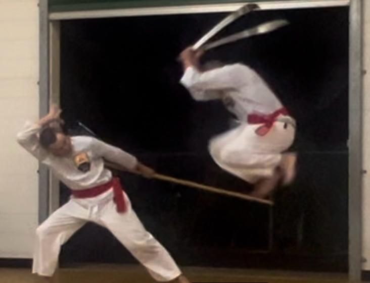 Two men are practicing martial arts and one is jumping in the air
