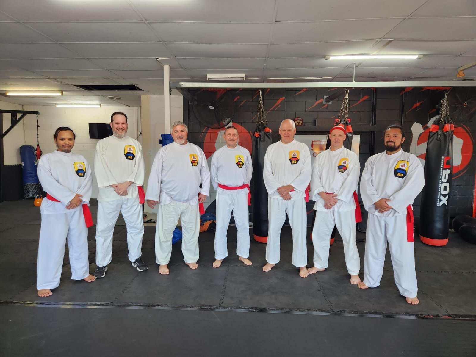 A group of men in white karate uniforms are posing for a picture in a gym.