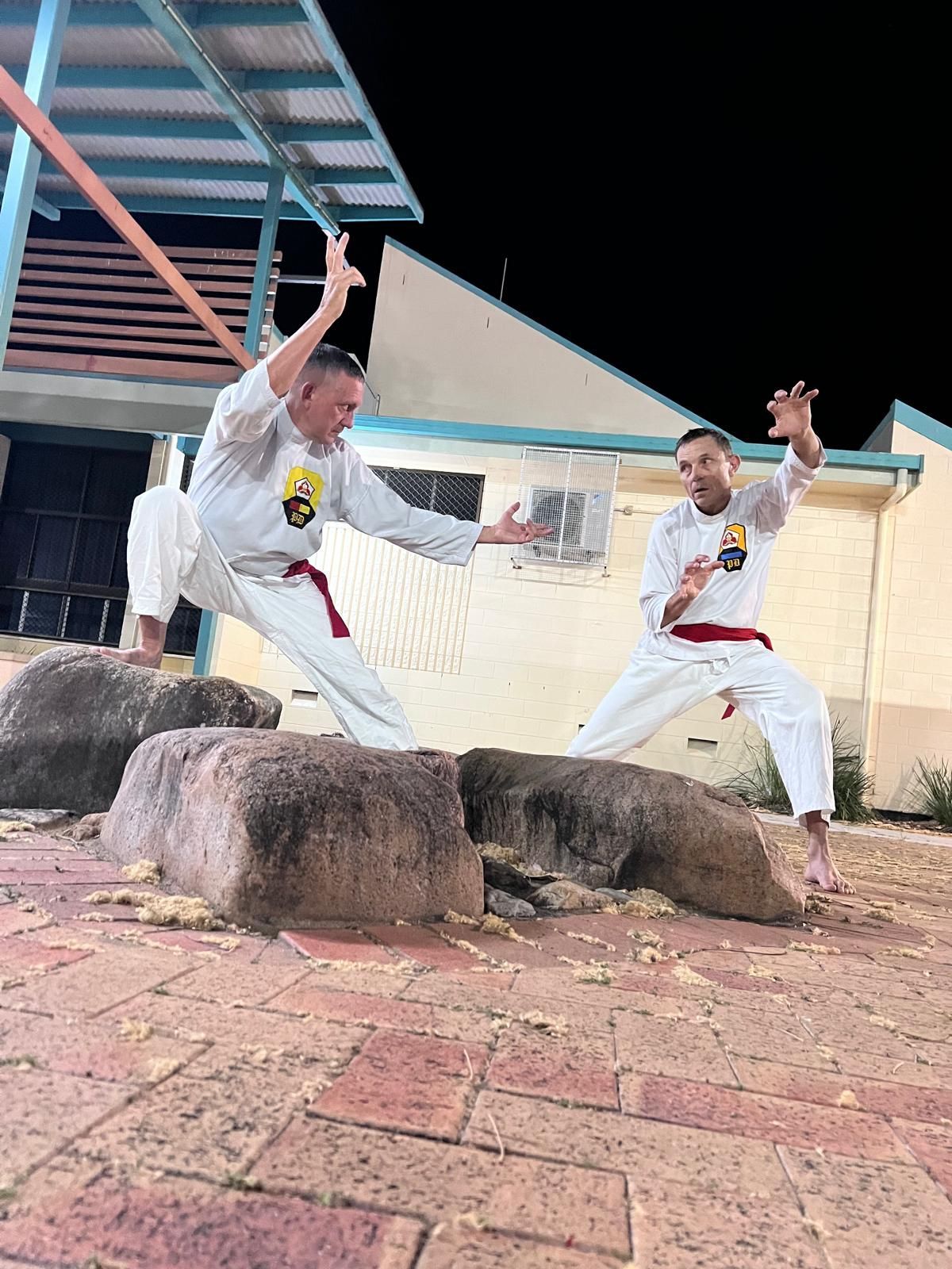 Two men are practicing karate on rocks in front of a building.