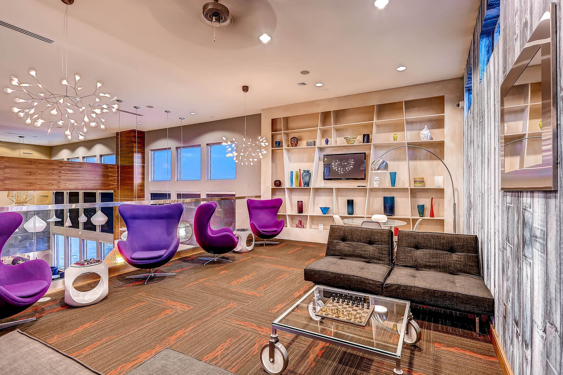 Modern community lounge with purple lounge chairs, a glass coffee table, and built-in shelving.