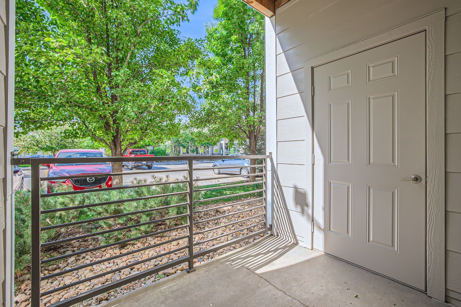 Balcony view from a ground-floor apartment door with a metal railing and green trees beyond.