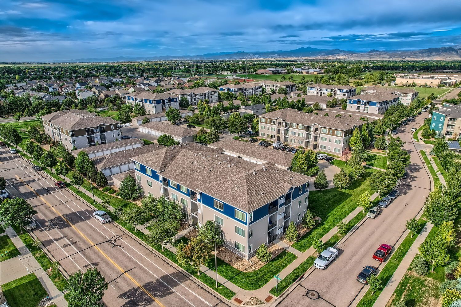 Aerial view of a multi-building apartment community with trees, roads, and parking.