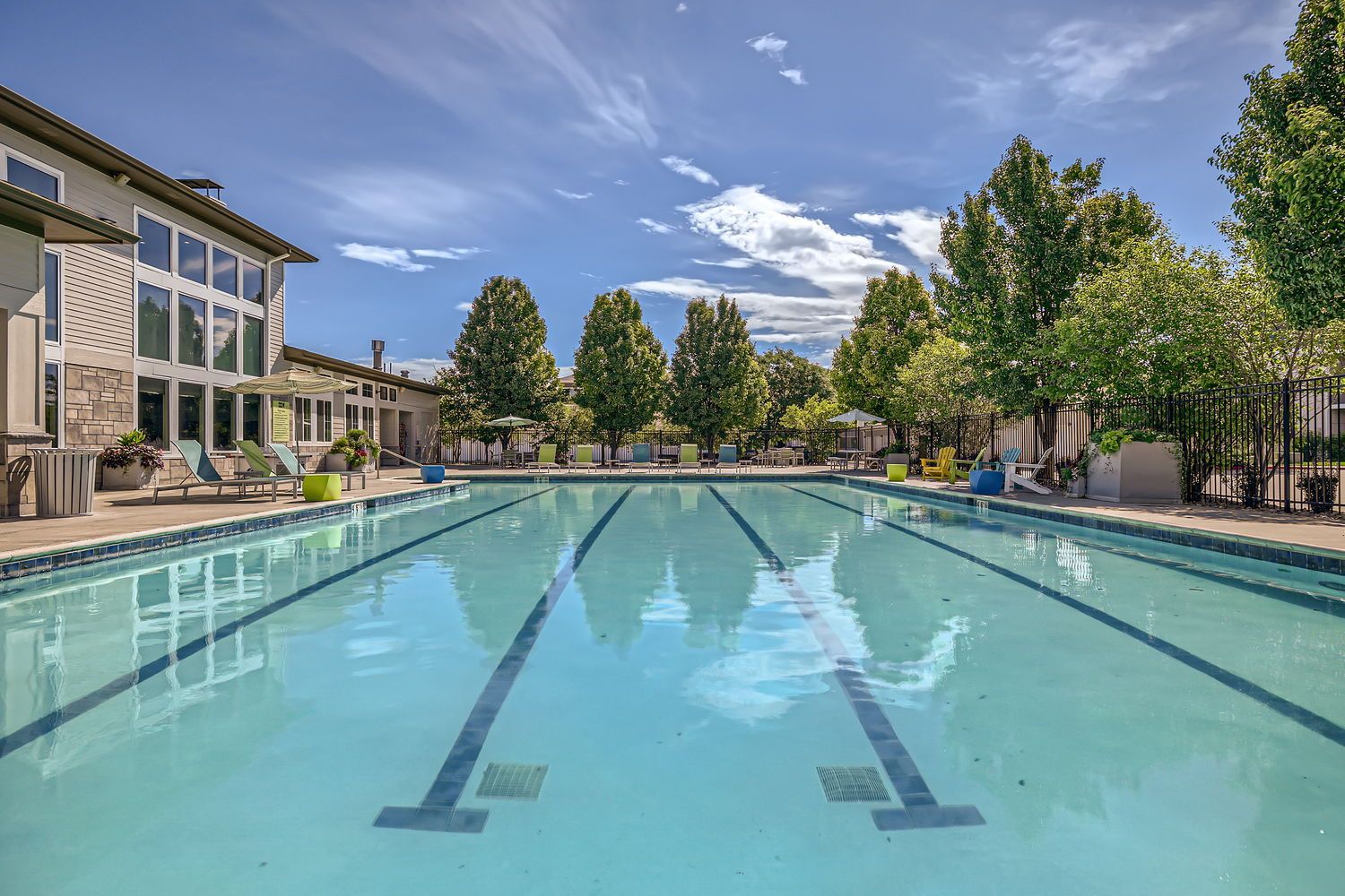Outdoor apartment community pool with lounge chairs and trees.