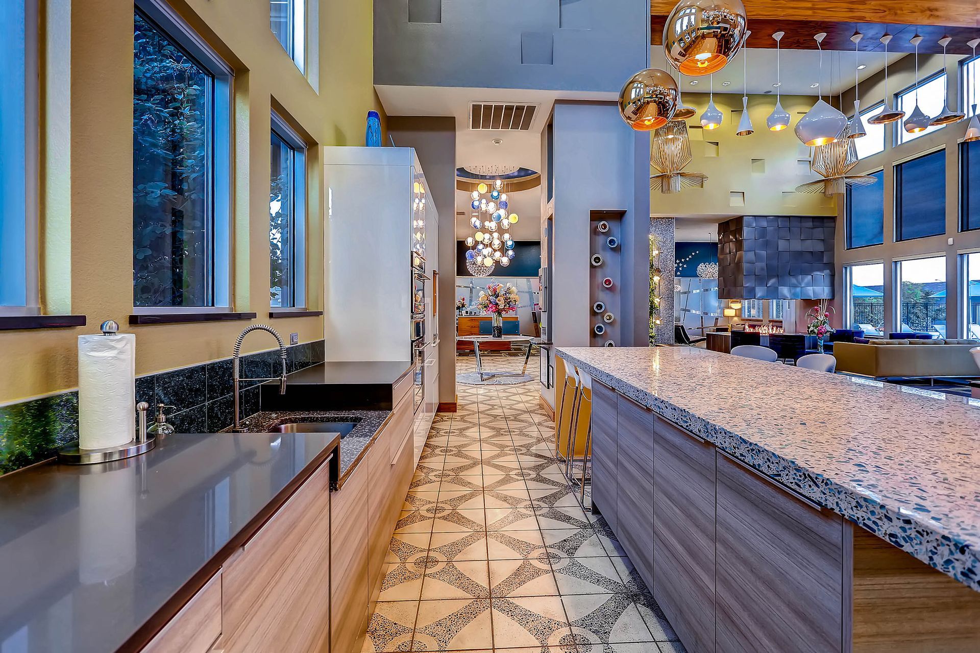 Bright community kitchen with a large granite island, stainless steel appliances, and pendant lights.