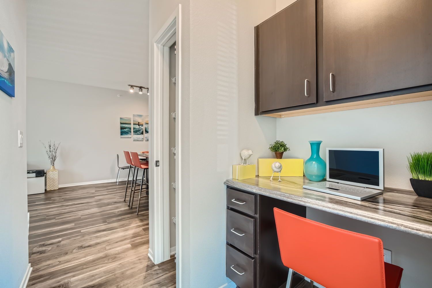 Home office nook in an apartment with desk, laptop, orange chair, and dark cabinets.