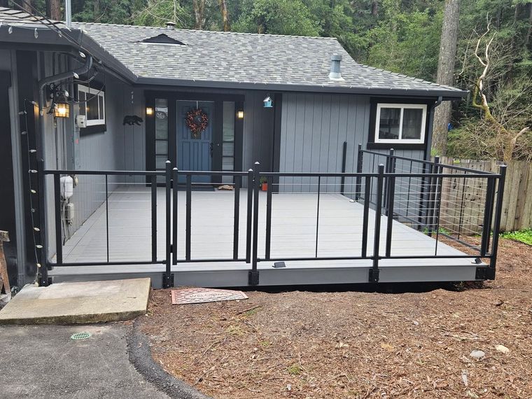 Gray cabin deck with black railing and steps in a wooded area