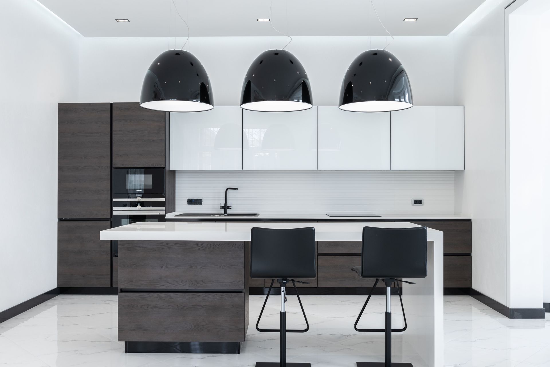 Modern minimalist kitchen with dark wood island, white cabinets, and black pendant lights