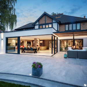 Modern two-story house with open patio, large glass doors, and outdoor seating at dusk