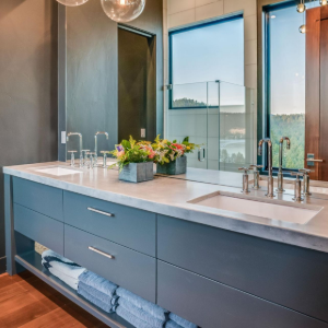 Modern bathroom vanity with dual sinks, blue cabinets, large mirror, and a flower arrangement