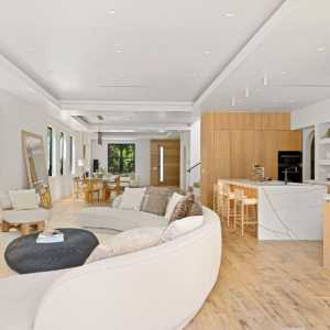 Modern open-plan living room and kitchen with curved white sofa, wood flooring, and light wood cabinetry.