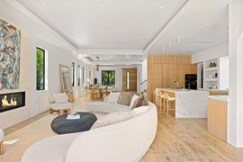 Bright modern living room with curved white sofa, fireplace, wood kitchen, and light oak floors