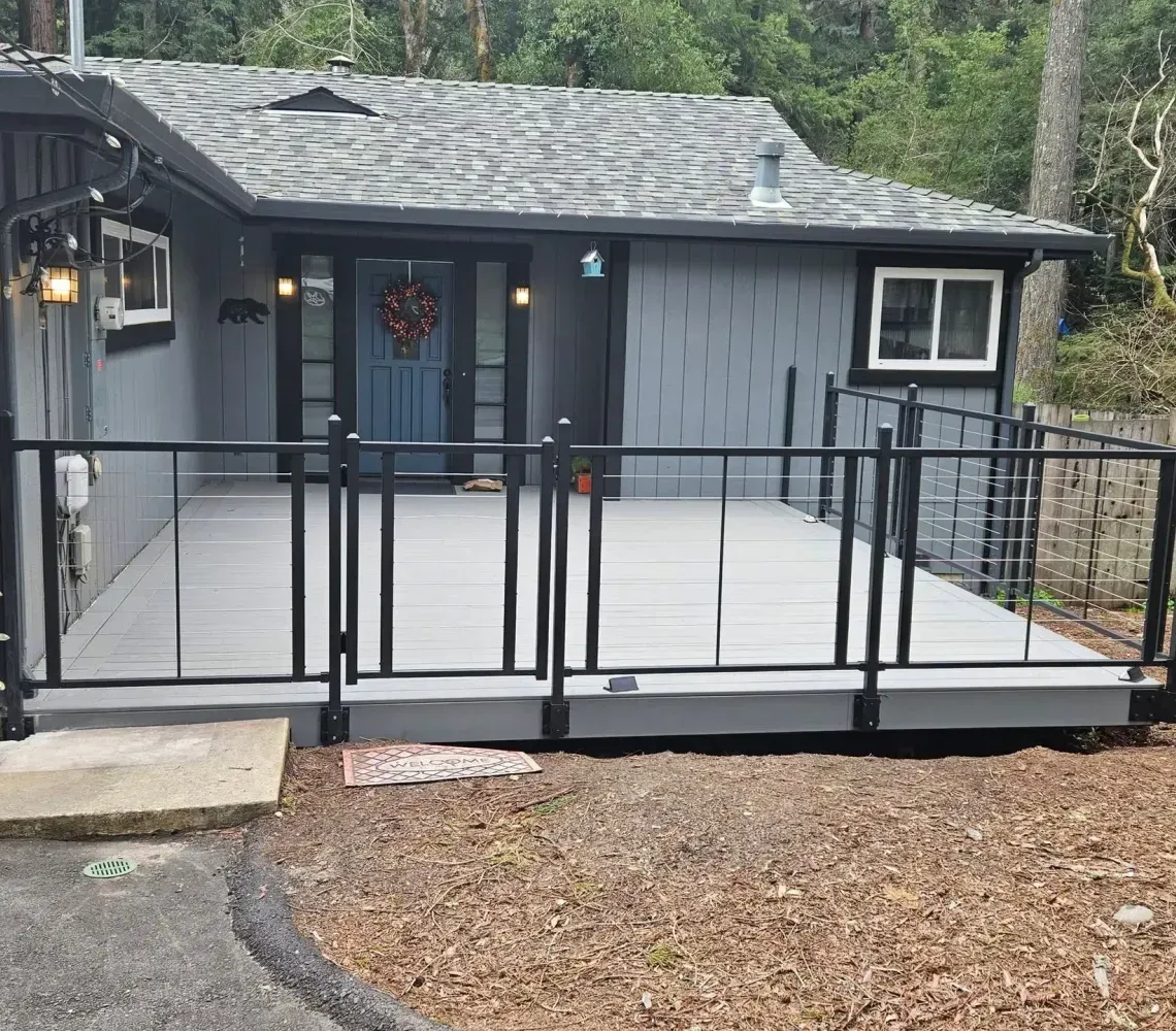 Gray cabin deck with black railing and steps in a wooded area