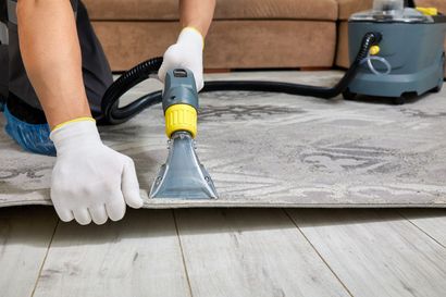 A person is cleaning a rug with a vacuum cleaner.