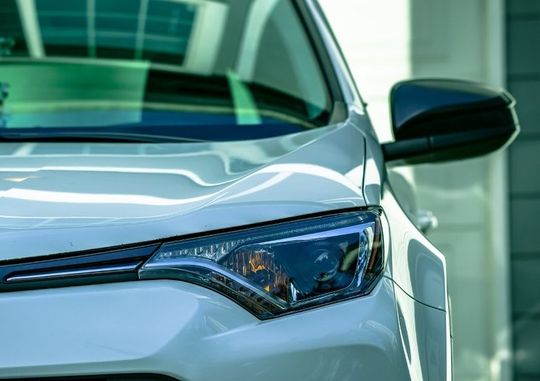 A close up of the headlight of a white car parked in front of a building.