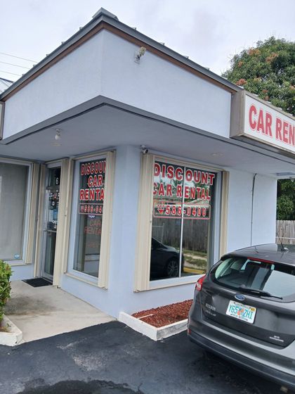 A car is parked in front of a car rental shop.