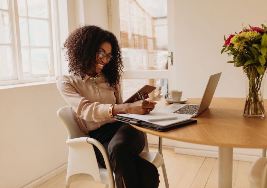 A woman is sitting at a desk with a laptop and a tablet.