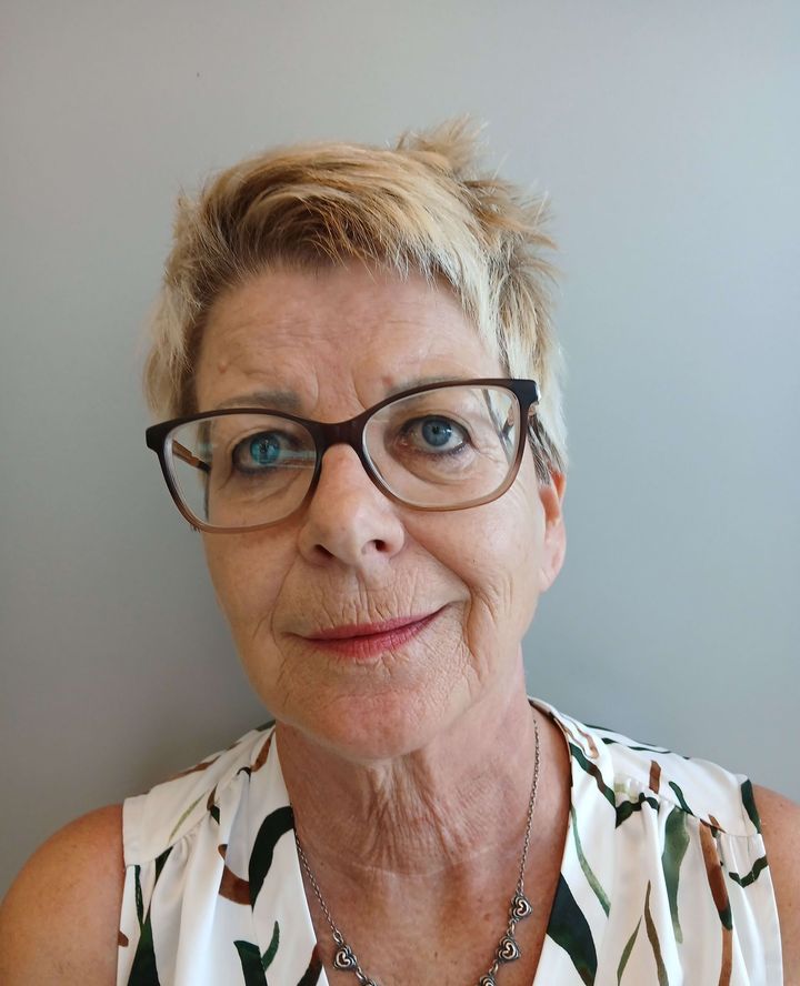A woman wearing glasses and a necklace is smiling for the camera.