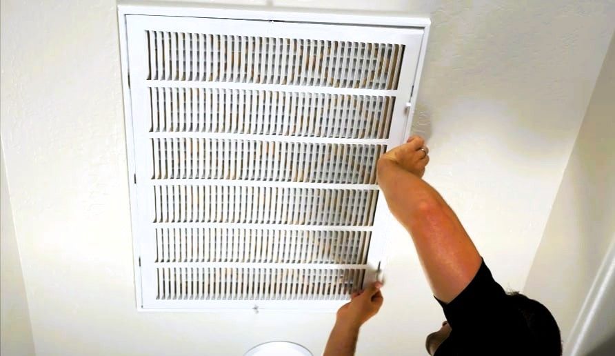 Person changing an air vent filter on the ceiling.