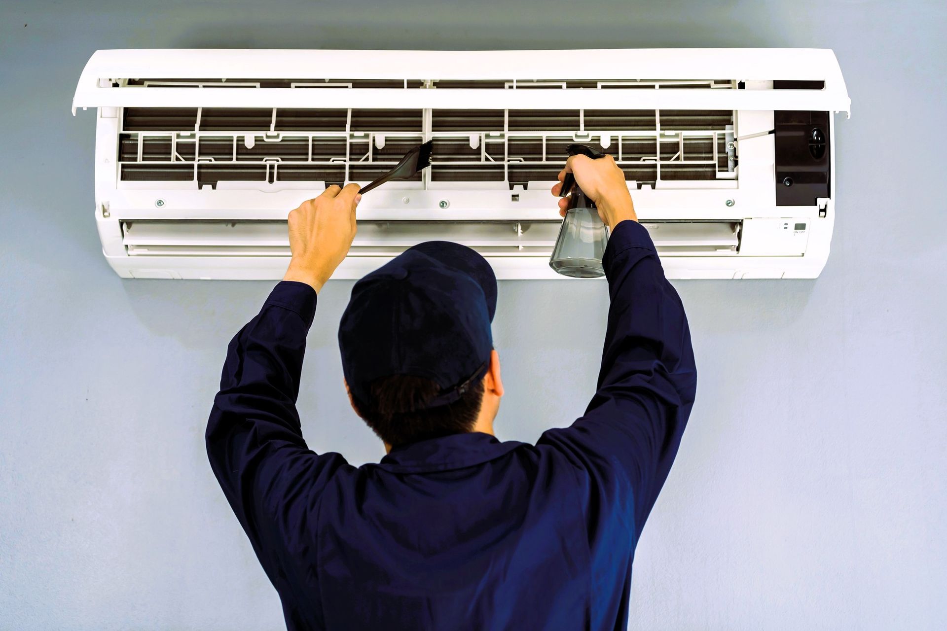 A technician is servicing an air conditioner unit mounted on a wall