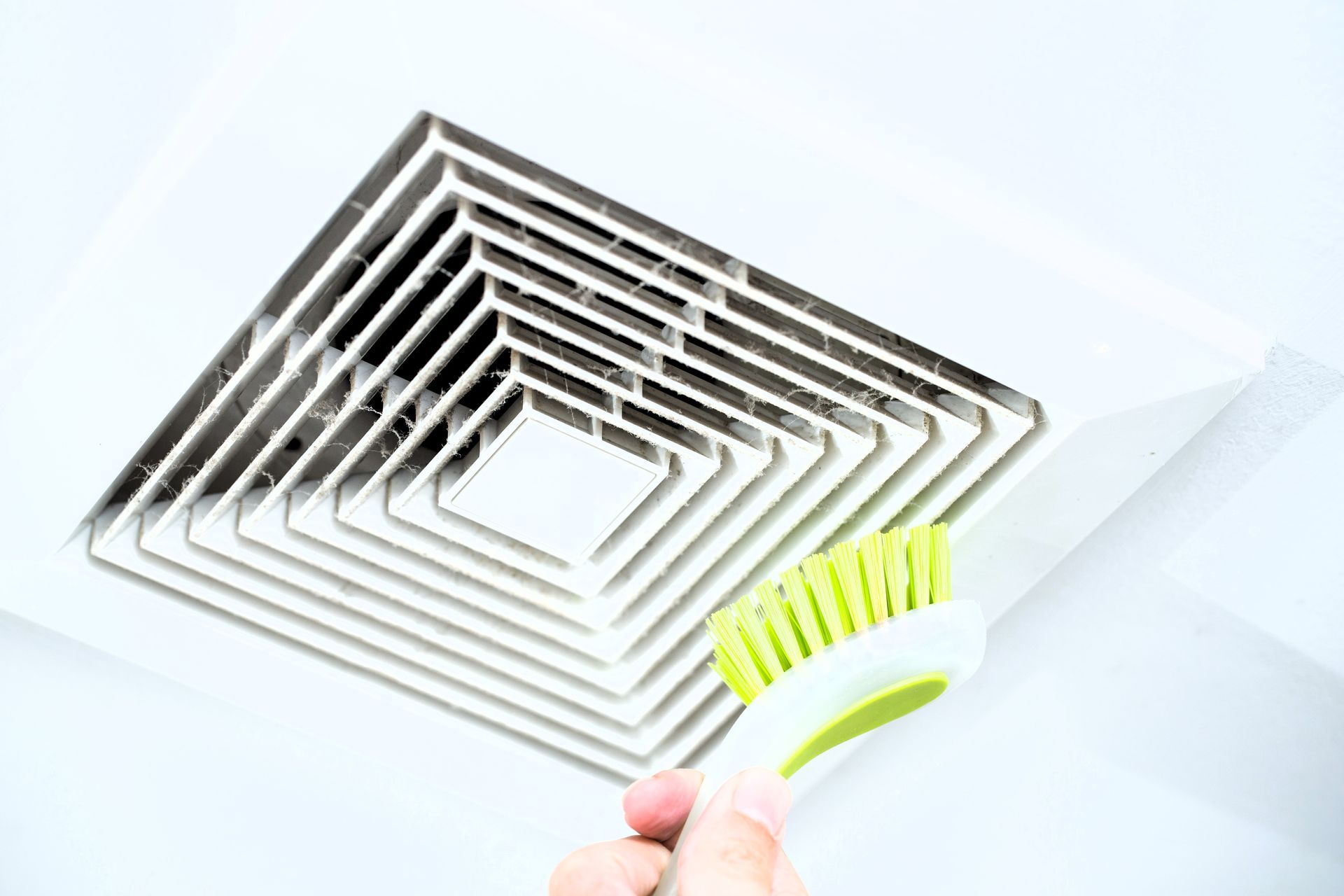 Person scrubbing a dusty ceiling vent with a green brush