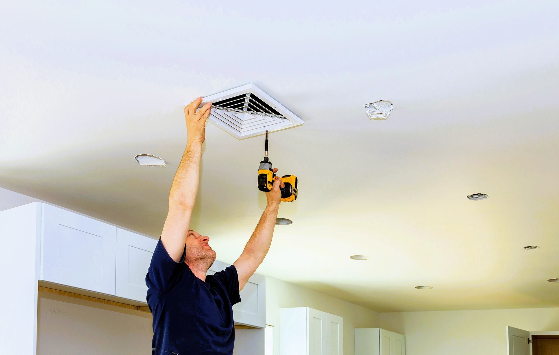 Person using a drill to install a vent cover on a ceiling.