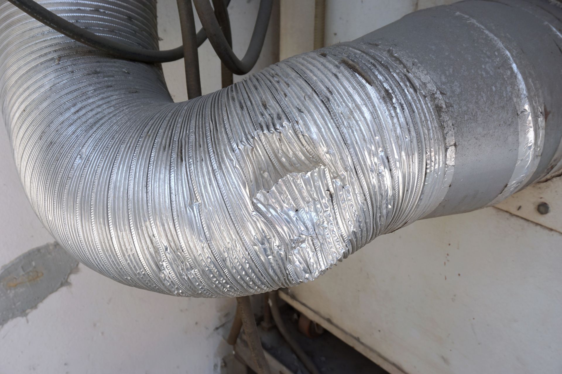 damaged flexible aluminum dryer vent duct with crimped section near corner