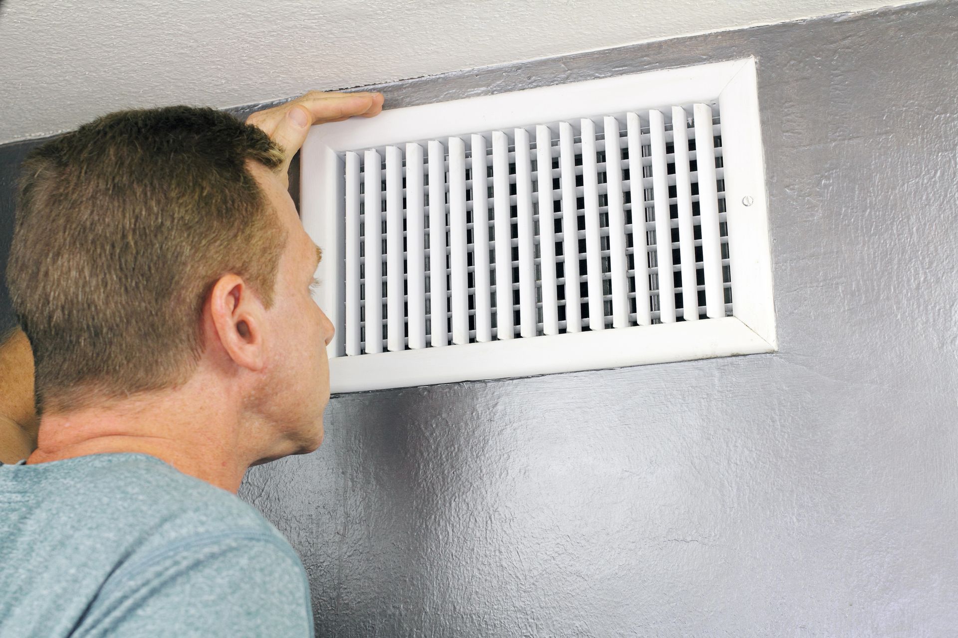 Technician inspecting a wall-mounted air vent for duct sanitization and odor removal.